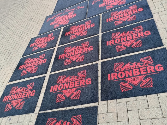 Vários tapetes Cleankap personalizados com a marca Ironberg, em vermelho sobre base escura, dispostos na calçada