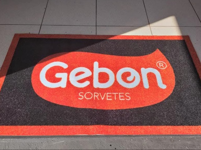 Tapete Cleankap da Gebon Sorvetes instalado no piso, com logotipo em laranja e branco e borda vermelha