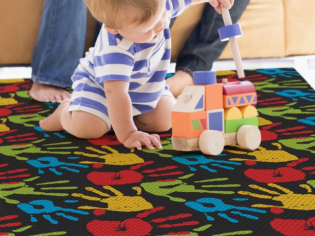 Bebê brincando com blocos de madeira sobre tapete infantil preto com estampa de palmas das mãos coloridas